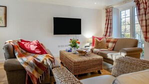 Ein Wohnzimmer mit Flachbildfernseher, einer Couch, einem Sessel, einem Couchtisch und einem Fenster mit Vorhängen.