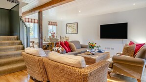 Ein geräumiges Wohnzimmer mit Rattanmöbeln, einem Flachbildfernseher und einer Treppe.