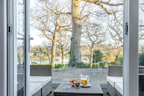 A dining area with wicker furniture, a table with breakfast items, and a view of trees and a body of water.