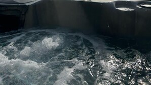 Ett bubbelbad med två flaskor och glas på kanten, omgivet av vatten.