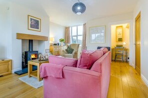 Un salon chaleureux avec une cheminée, un canapé rose, une table basse en bois et un coin repas comprenant une chaise et une table.