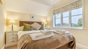 A neatly made bed with pillows, a bedside lamp, and a window with a view.
