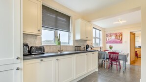 A modern kitchen with white cabinets, a black countertop, and a dining area with a red chair and table.