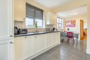 A modern kitchen with white cabinets, a black countertop, and a dining area with a red chair and table.