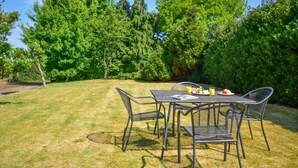An outdoor dining area with a table and chairs, surrounded by lush greenery and trees.
