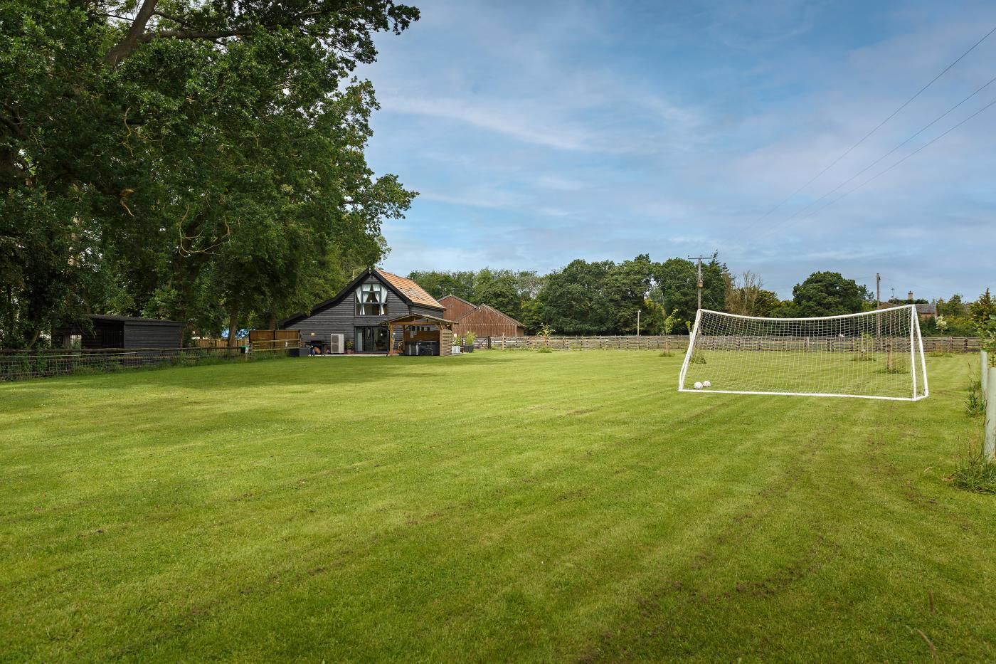 Ein gepflegtes Rasenfeld mit einem Fußballtor, einem Holunderstall und einem Haus im Hintergrund.