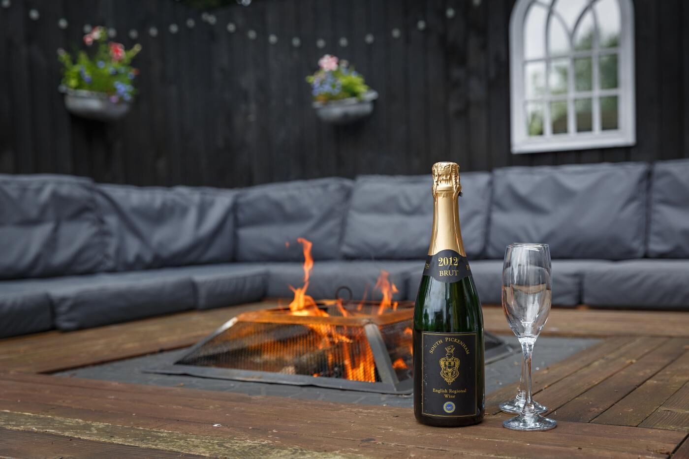 Eine Flasche 2012 Brut Champagner, ein Glas und eine Feuerstelle auf einem Holztisch.