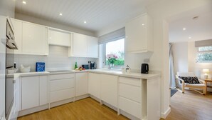 Una cocina moderna con armarios blancos, piso de madera y ventana con vistas a la vegetación.
