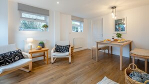 Una sala de estar acogedora con un sofá, una silla, una mesita con una lámpara y un comedor con una mesa lista para el desayuno.