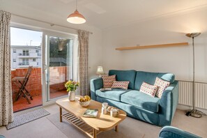 Un salon avec un canapé, une table basse et une vue sur l’extérieur, accessible par une porte-fenêtre coulissante.