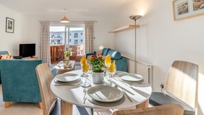 Sala moderna com uma mesa de jantar para dois, sofá, televisão e vista para edifícios através de grandes janelas.