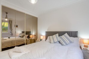 Une chambre d’hôtel avec un grand miroir, un lit recouvert de draps blancs, des oreillers à rayures et des lampes de chevet.