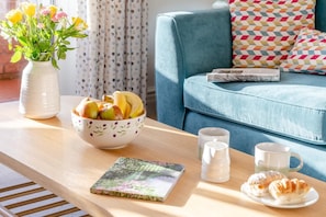 Une table en bois sur laquelle se trouvent un saladier rempli de fruits, un livre, deux tasses et des pâtisseries.