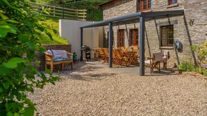 A stone building with a covered patio, outdoor seating, and a grill.
