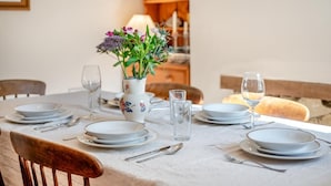 A dining table set with plates, glasses, and cutlery, a vase with flowers, and a loaf of bread. - 3 Bed in Swanage (oc-s30316) (Swanage)
