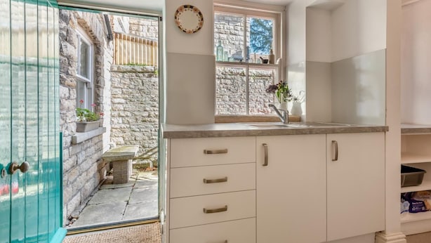 A kitchen with white cabinets, a sink, and a window overlooking a stone wall. - 3 Bed in Swanage (oc-s30316) (Swanage)