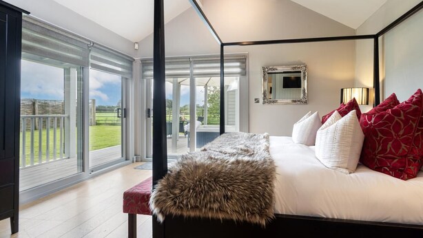Ein Schlafzimmer mit einem großen Bett, einem Fellüberwurf und Blick auf einen Garten durch Glastüren.
