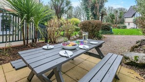 A picnic table with plates, cutlery, and a bowl of fruit in a garden setting. - 3 Bed in St. Ives (oc-c30315) (Carbis Bay)