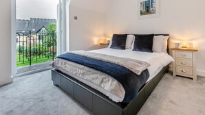 A bedroom with a bed, bedside tables, a window with a view of greenery, and a painting on the wall. - 3 Bed in St. Ives (oc-c30315) (Carbis Bay)