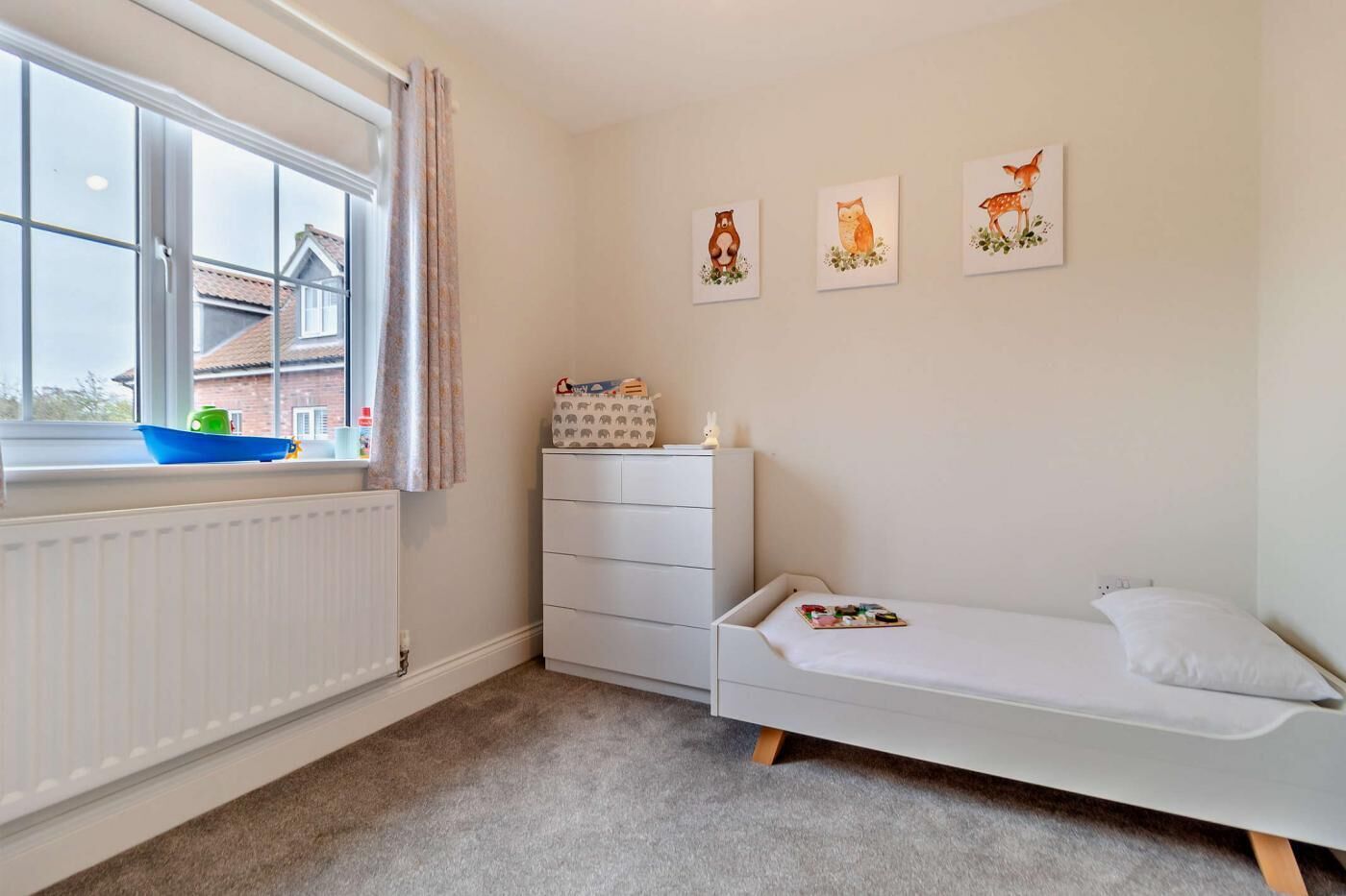 Ein Kinderzimmer mit Fenster, einer weißen Kommode, einem Einzelbett und drei Wandbildern mit Tiermotiven.