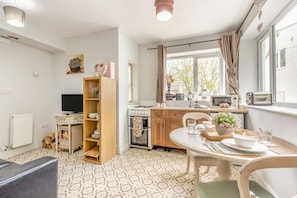 Una cocina compacta con estufa, microondas y tostadora. Hay una mesa de comedor con sillas y un mueble pequeño con vajilla.