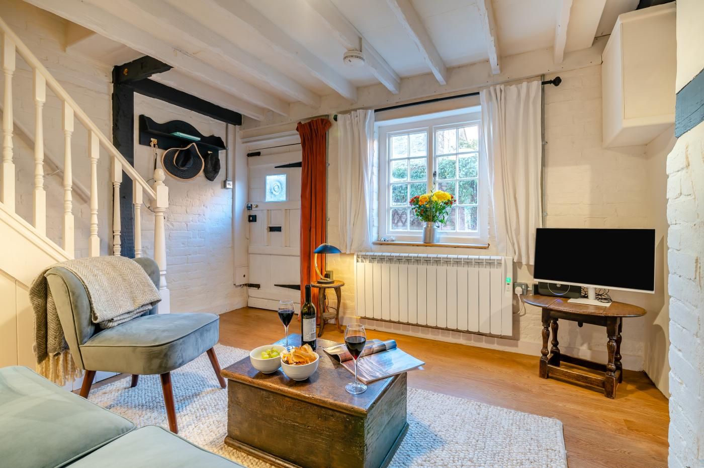 En hyggelig stue med sofa, sofabord med mad og drikke, TV og et vindue med gardiner.