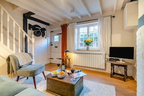 Ein gemütliches Wohnzimmer mit einer Couch, einem Couchtisch mit Speisen und Getränken, einem Fernseher und einem Fenster mit Vorhängen.