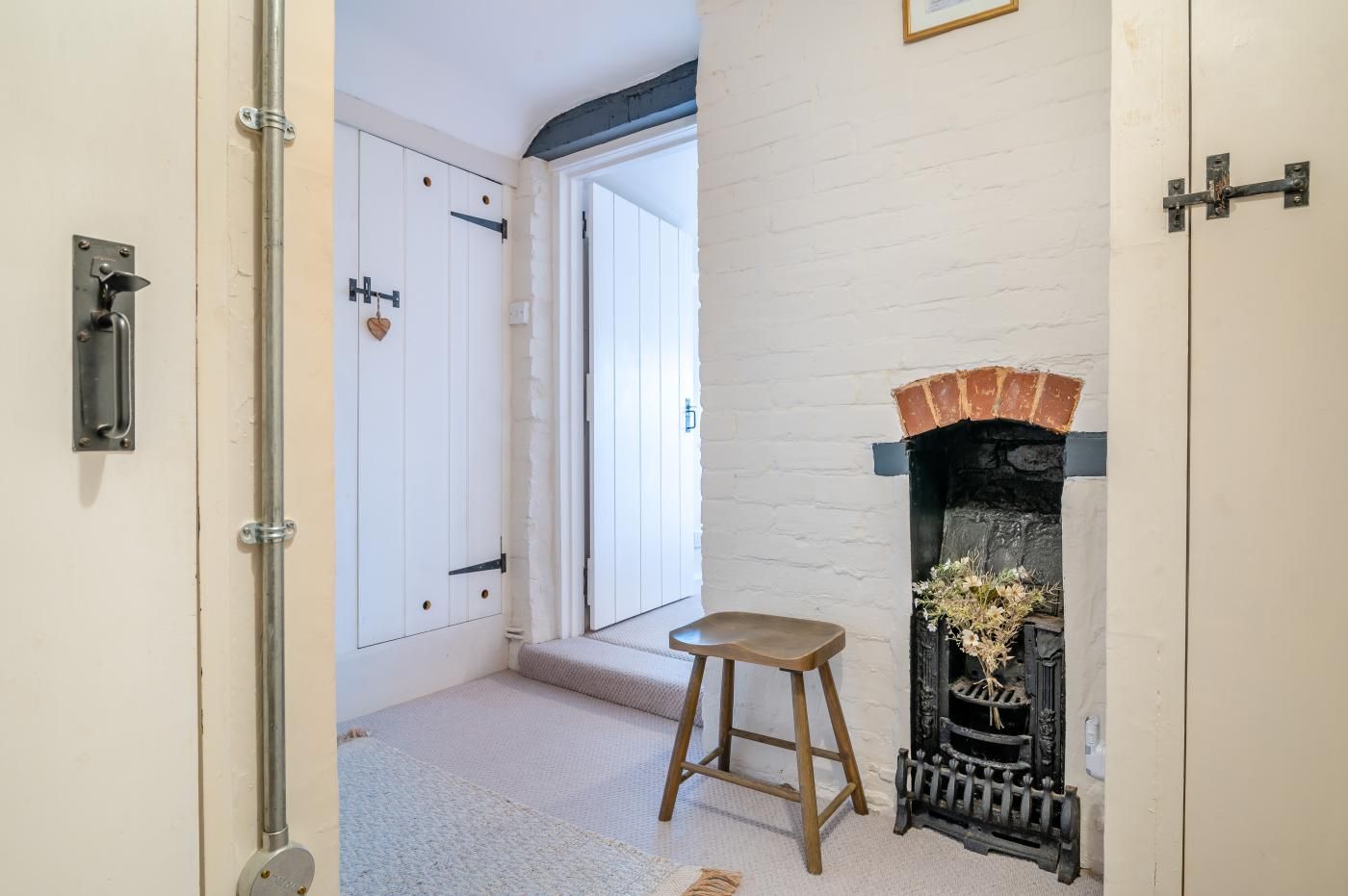 Une pièce avec une porte blanche, une cheminée encadrée de briques et un petit tabouret en bois.