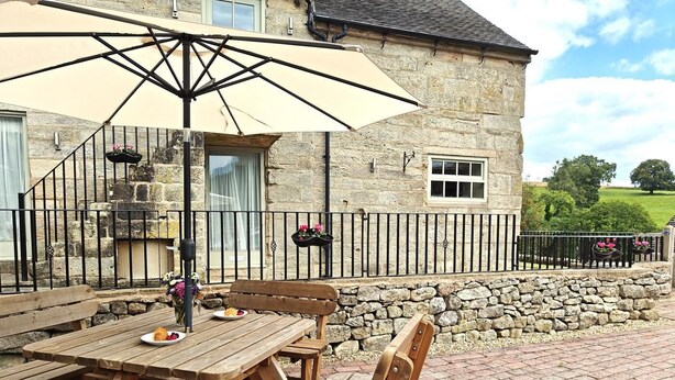 A stone building with a stone wall and a wooden bench. - 2 Bed in Ellastone (oc-t30011) (Ellastone)