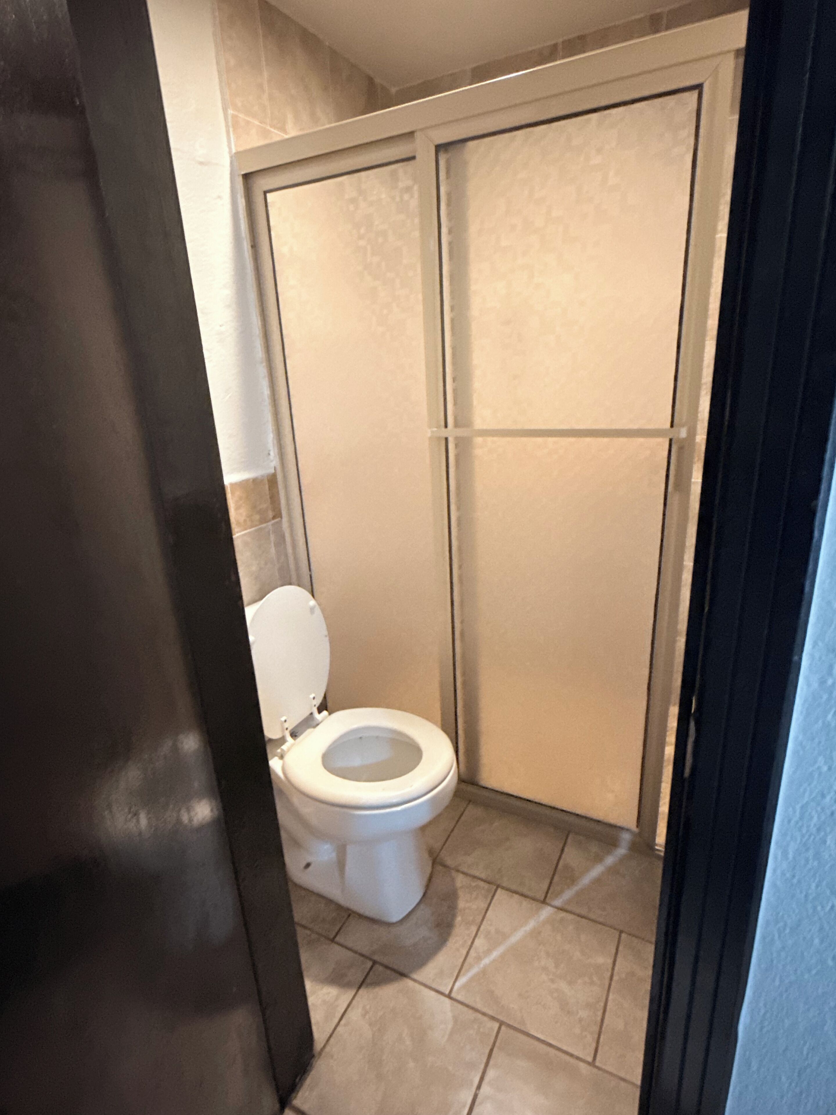 Un baño con inodoro, cabina de ducha y suelo de baldosas.