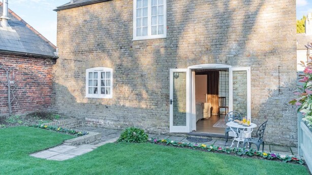 A two-story stone house with a small front garden, a patio with outdoor furniture, and a door leading to an interior room. - 1 Bed in Sutton (oc-u30398) (Sutton)