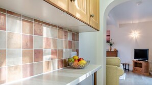 A kitchen with a tiled backsplash, a fruit bowl on the counter, and a living area with a sofa and TV. - 1 Bed in Sutton (oc-u30398) (Sutton)