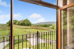 A balcony with a view of a green landscape, including trees and hills.
