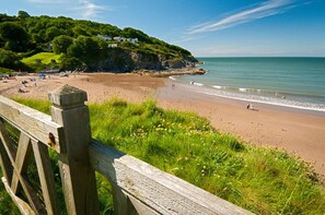 A beach with a wooden fence, grassy areas, and a cliff with houses.