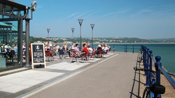 A waterfront dining area with outdoor seating, a signboard, and a bicycle parked by the railing. - 3 Bed in Pontardawe (oc-c30415) (Cilybebyll Pontardawe)