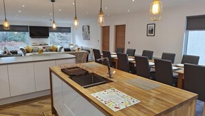 A modern kitchen with a central island, dining area with chairs, pendant lighting, and a view of the outdoors. - 7 Bed in Colintraive (oc-d30232) (Colintraive)