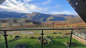 A balcony with a view of a mountainous landscape, a grassy area with rocks, and a small pond. - 7 Bed in Colintraive (oc-d30232) (Colintraive)