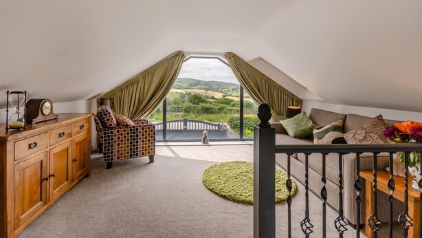 Un dormitorio acogedor en el ático con vistas a colinas ondulantes, un aparador de madera, un sillón estampado y un sofá con cojines.