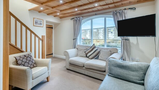 Ein Wohnzimmer mit Holzboden, einem Sofa, einem Sessel, einem Fernseher und einem Fenster mit Vorhängen.
