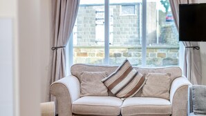 Ein beiges Sofa mit gestreiften Kissen, ein Flachbildfernseher und ein Fenster mit Vorhängen.