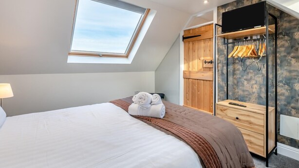 Ein Schlafzimmer mit Dachfenster, einem Bett mit aufgerollten Handtüchern, einem Holzschrank und einer Kleiderstange.