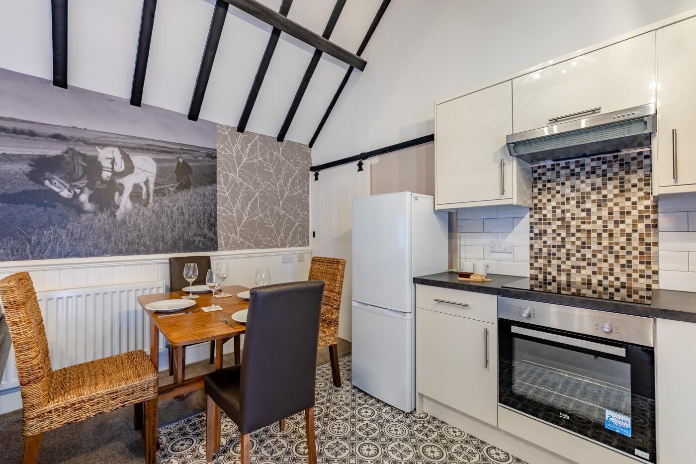 Una cocina compacta con comedor, que cuenta con una estufa moderna, gabinetes blancos y un salpicadero decorativo.