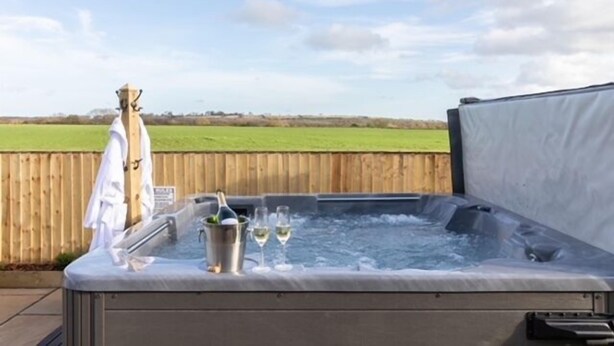 Un jacuzzi con terraza de madera, una botella de champán y dos copas de vino.