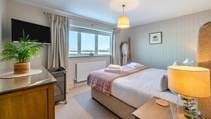 Habitación de hotel con cama, mesita de noche, lámpara, planta en maceta y vistas al exterior.