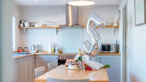 Una cocina moderna con una mesa de madera dispuesta para una celebración, mostrando un pastel, champán y flores.