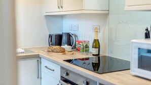Una cocina moderna con armarios blancos, un hervidor de acero inoxidable, una hogaza de pan, una botella de vino y una caja de té Yorkshire Tea.