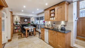 A kitchen with wooden cabinets, a dining table set for four, and a black kettle on the counter. - 2 Bed in West Burton (oc-i30367) (West Burton)