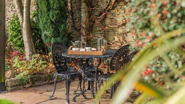 An outdoor table with chairs, a tray with teapots and cups, and a stone wall in the background. - 2 Bed in West Burton (oc-i30367) (West Burton)