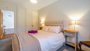 Ein Schlafzimmer mit einem Bett, Nachttischen, einer Lampe, einem Kleiderschrank und einem Fenster.