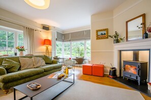A cozy living room with a green sofa, a coffee table, a fireplace, and large windows. - 5 Bed in Church Stretton (oc-t30413) (Church Stretton)